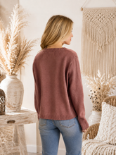 Load image into Gallery viewer, A woman wearing a dusty rose knit sweater and blue jeans, shown from the back in a warm, bohemian-style room with dried pampas grass and a macrame wall hanging.
