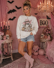 Load image into Gallery viewer, A woman stands in a pink Halloween-themed room wearing a white long-sleeve sweatshirt with a ghost and pumpkin graphic, denim shorts, and pink cowboy boots.