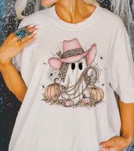 Load image into Gallery viewer, A woman wearing a white graphic t-shirt featuring a cartoon ghost wearing a pink cowboy hat with a leopard print bandana, surrounded by pumpkins and a lasso.
